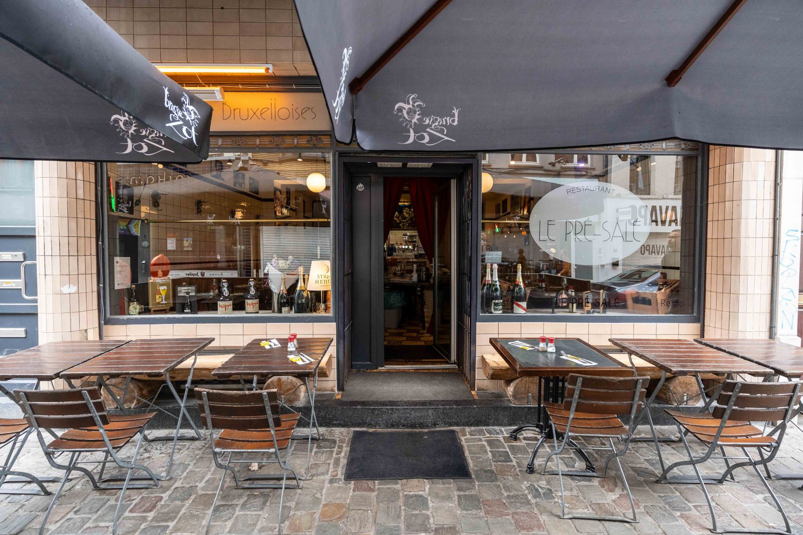 Façade et entrée du Pré Salé avec stores noirs et tables en terrasse, spécialités bruxelloises