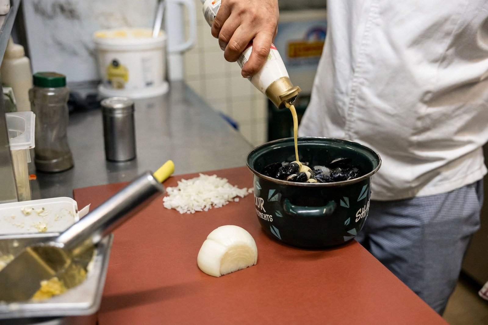 O cozinheiro do Le Pré Salé rega os mexilhões frescos na panela esmaltada verde, com cebolas picadas ao lado