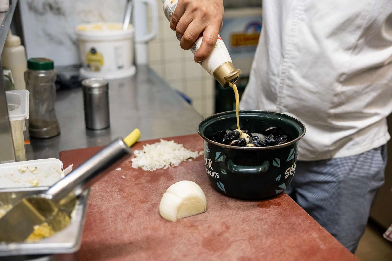 Le cuisinier du Pré Salé arrose les moules fraîches dans la casserole émaillée verte, oignons émincés à côté